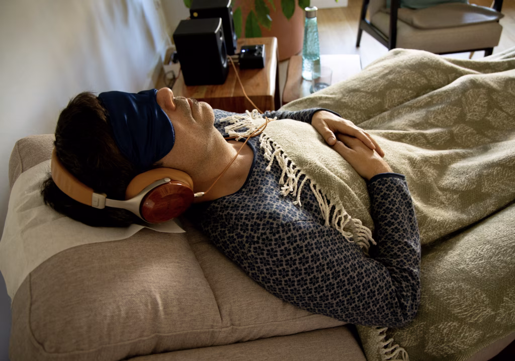 Hombre tumbado en un sofá con antifaz, auriculares y una manta