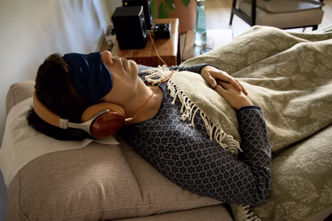 Hombre tumbado en un sofá con antifaz, auriculares y una manta