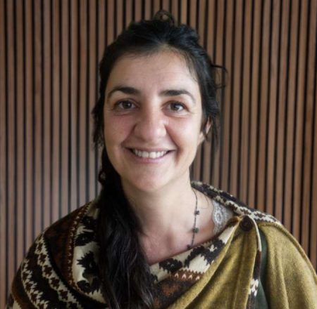 Smiling person wearing patterned shawl indoors.