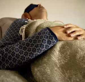 Man reclining with an eye mask, hands resting on a blanket
